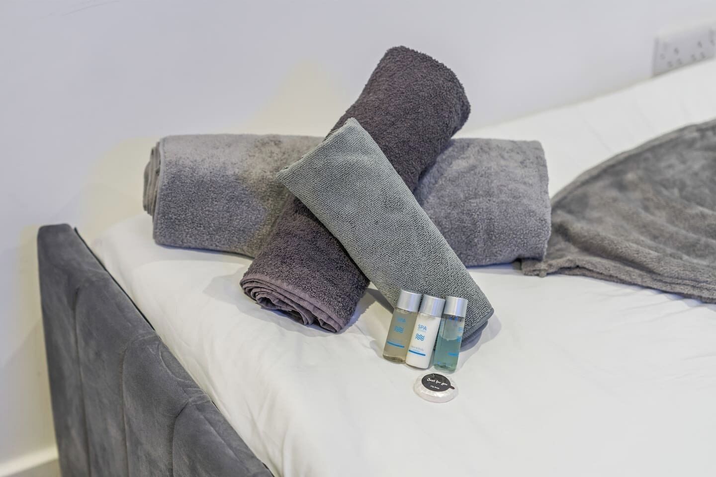 A bed with grey towels and a bottle of lotion.