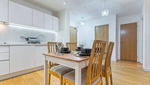 Uma cozinha moderna com armários brancos, uma mesa de jantar posta para quatro pessoas e piso de madeira.