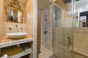 Een badkamer met een witte wasbak, een spiegel met gouden lijst en een douche met een wand van kiezelsteentjes.