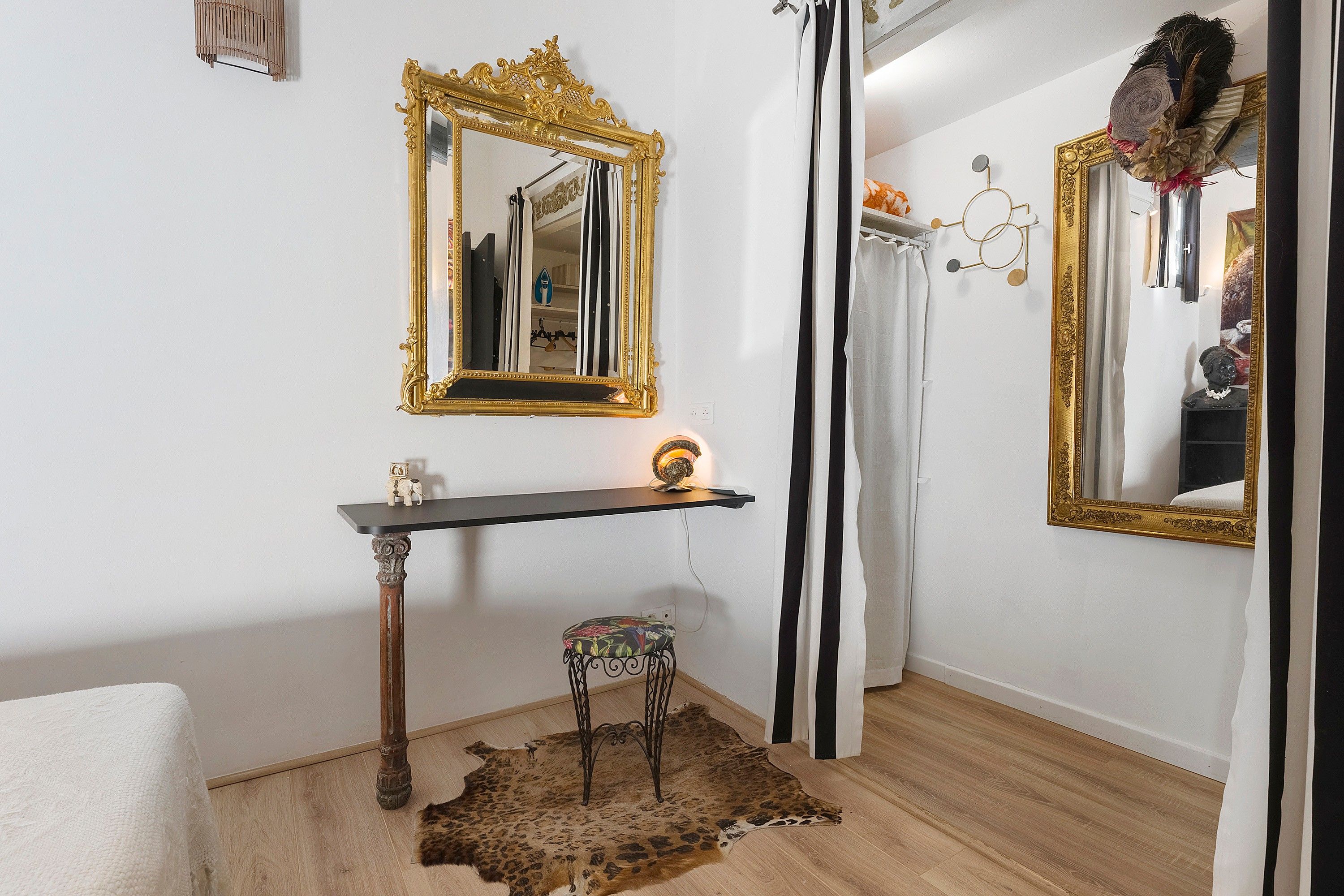 Une pièce comprenant un grand miroir décoratif, une petite table ornée d’un objet décoratif, un tapis en fourrure et une chaise.