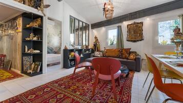 Ein helles Wohnzimmer mit einem roten Sessel, einer Couch und einem Esstisch für zwei Personen.