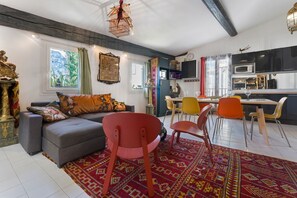 Un salon comprenant un canapé, des fauteuils, un tapis à motifs et un coin repas avec une table et des chaises.