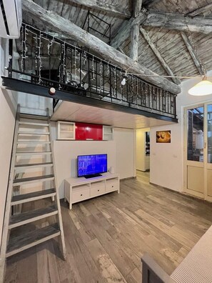 A loft-style room with a wooden floor, a TV, a staircase, and a balcony with a railing. - Terrace & Relax | Rome Collection (Roma)