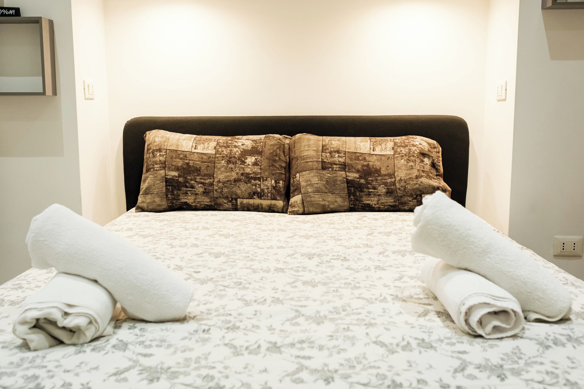 A neatly made bed with a floral bedspread and two rolled towels.