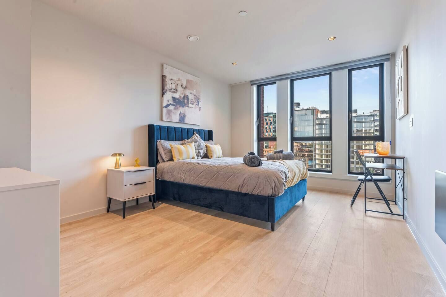 Een moderne slaapkamer met een groot bed, een nachtkastje, een stoel en uitzicht op de stad door grote ramen.