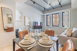 A modern dining area with a table set for four, a sofa, and a television in the background. - #179 Chic Birmingham City Escape - Sleeps 4 (West Midlands)