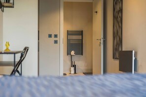Hotelkamer met een bed, een klein tafeltje met een stoel, een radiator aan de muur, en een deur naar een andere kamer.