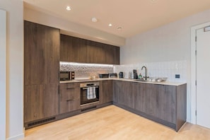 A modern kitchen with dark wood cabinetry, a microwave, an oven, and a sink. - #179 Chic Birmingham City Escape - Sleeps 4 (West Midlands)