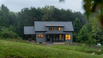 Een modern huis met twee verdiepingen, een overdekte veranda en een klein bijgebouw.