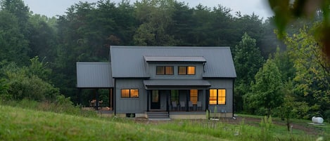 Una casa moderna de dos pisos con porche cubierto y una construcción separada.