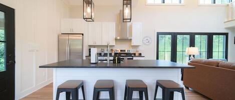 A modern kitchen with a central island, bar stools, and a dining area with a sofa.