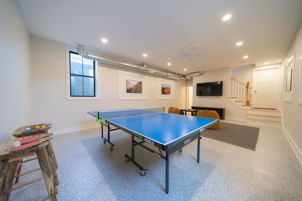 A ping pong table in a room with a staircase, a television, and artwork on the walls.
