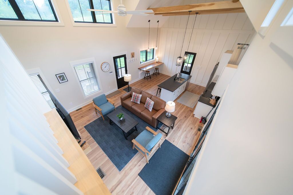 Un'ampia zona giorno in stile loft, con soffitto alto, area salotto centrale con divano e poltrone, cucina con bancone e ampie finestre che lasciano entrare luce naturale.