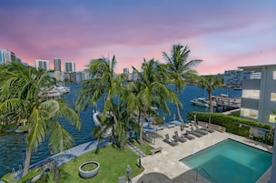 A waterfront property with a pool, lounge chairs, and palm trees.