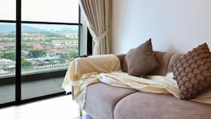 Ein Zimmer mit großem Fenster, einer Couch und Blick auf eine Stadtlandschaft.