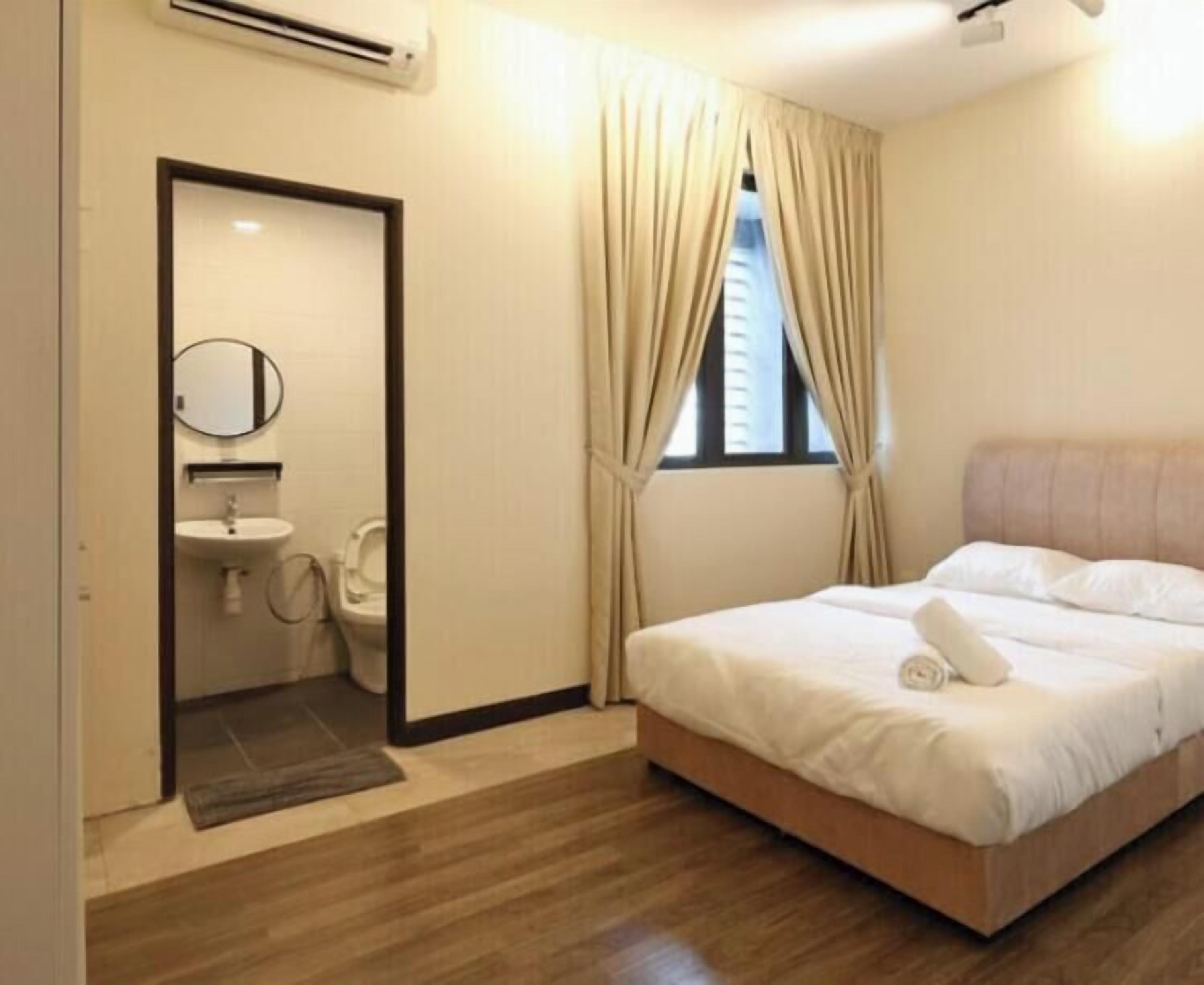 Un dormitorio con cama, ventana con cortinas, mesita de noche y baño con lavamanos y espejo.