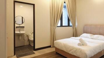 Un dormitorio con cama, ventana con cortinas, mesita de noche y baño con lavamanos y espejo.