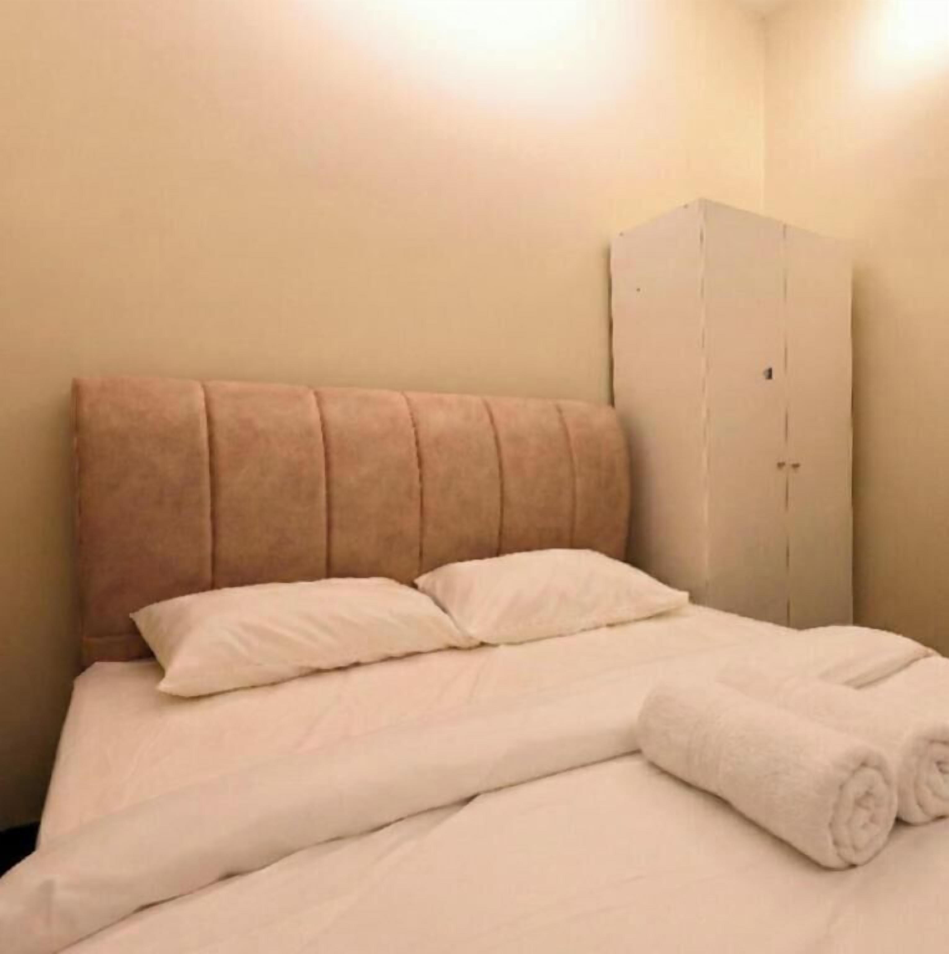 Un lit simple avec une tête de lit, deux oreillers et des serviettes enroulées.