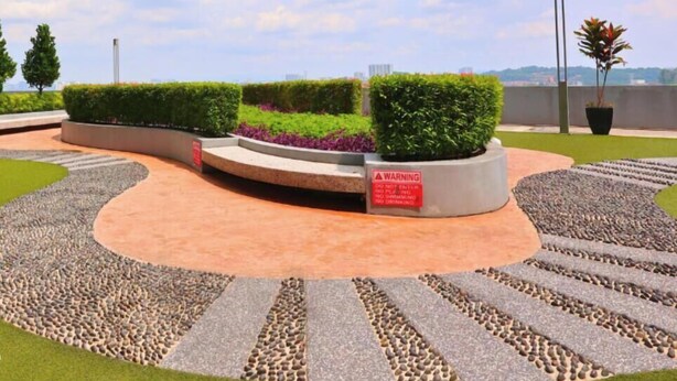 Área externa ajardinada com um caminho sinuoso, sebes bem aparadas e uma placa de aviso.