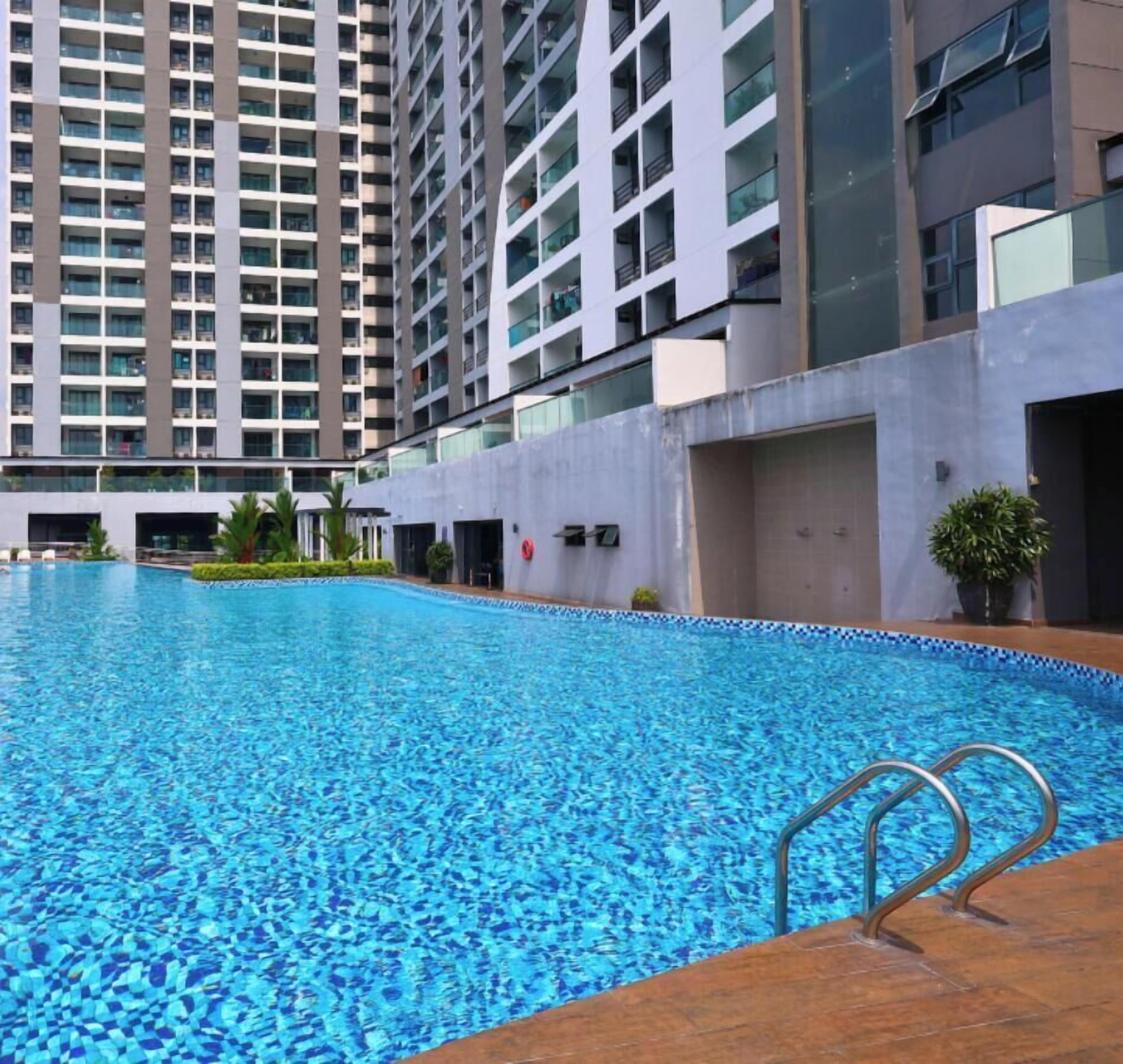 A swimming pool with a wooden deck and metal handrails, surrounded by a modern building with balconies.
