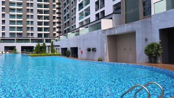 A swimming pool with a wooden deck and metal handrails, surrounded by a modern building with balconies.