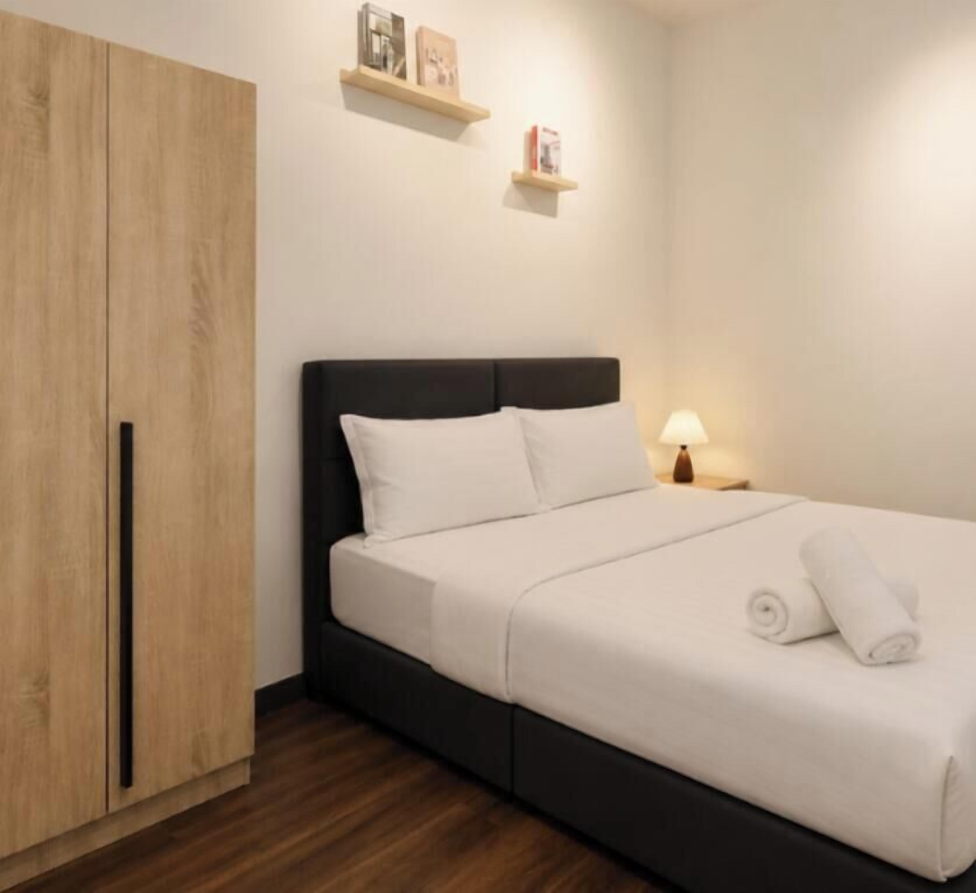 A bedroom with a bed, a wardrobe, a nightstand, and a wall-mounted shelf.