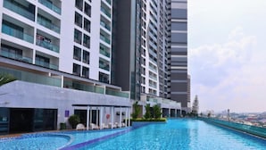 Piscina com borda azulejada, cercada por edifícios modernos e céu claro.