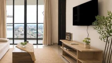 A modern living room with a large window, a flat-screen TV, a sofa, a coffee table, and a potted plant.