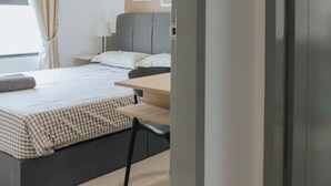 Una habitación de hotel con cama, mesita de noche y ventana con cortinas.