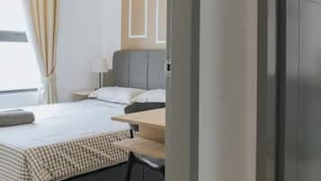A hotel room with a bed, bedside table, and a window with curtains.