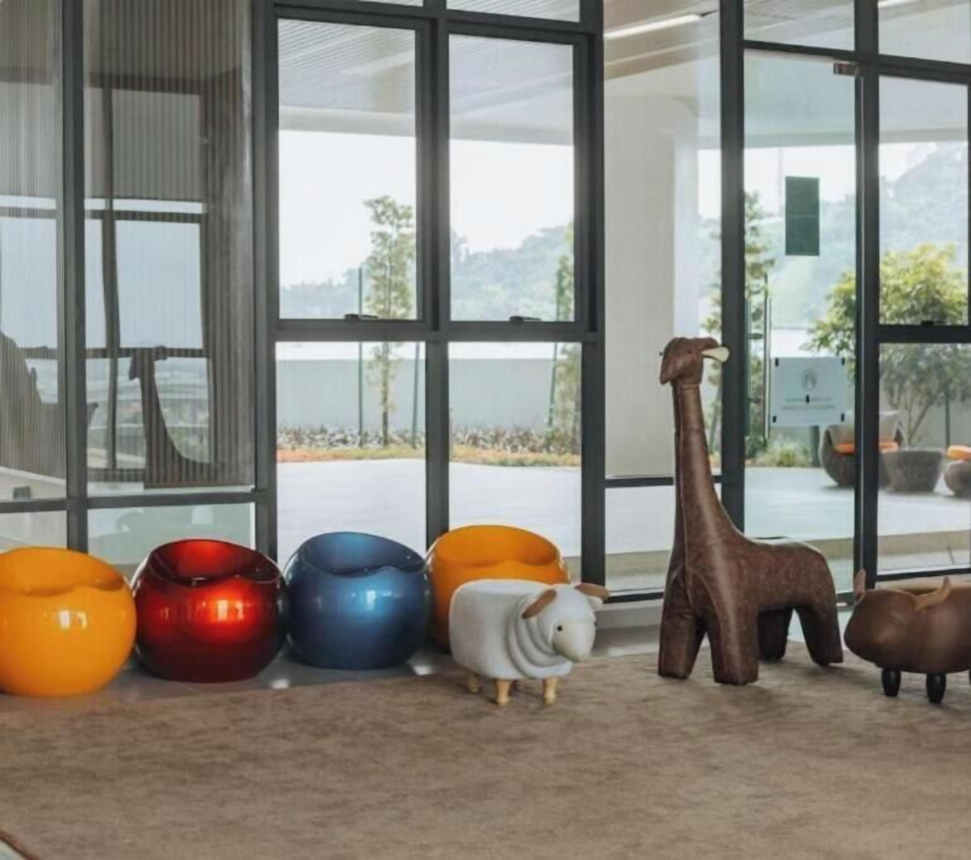 A room with large windows, a giraffe sculpture, and colorful animal-shaped vases.