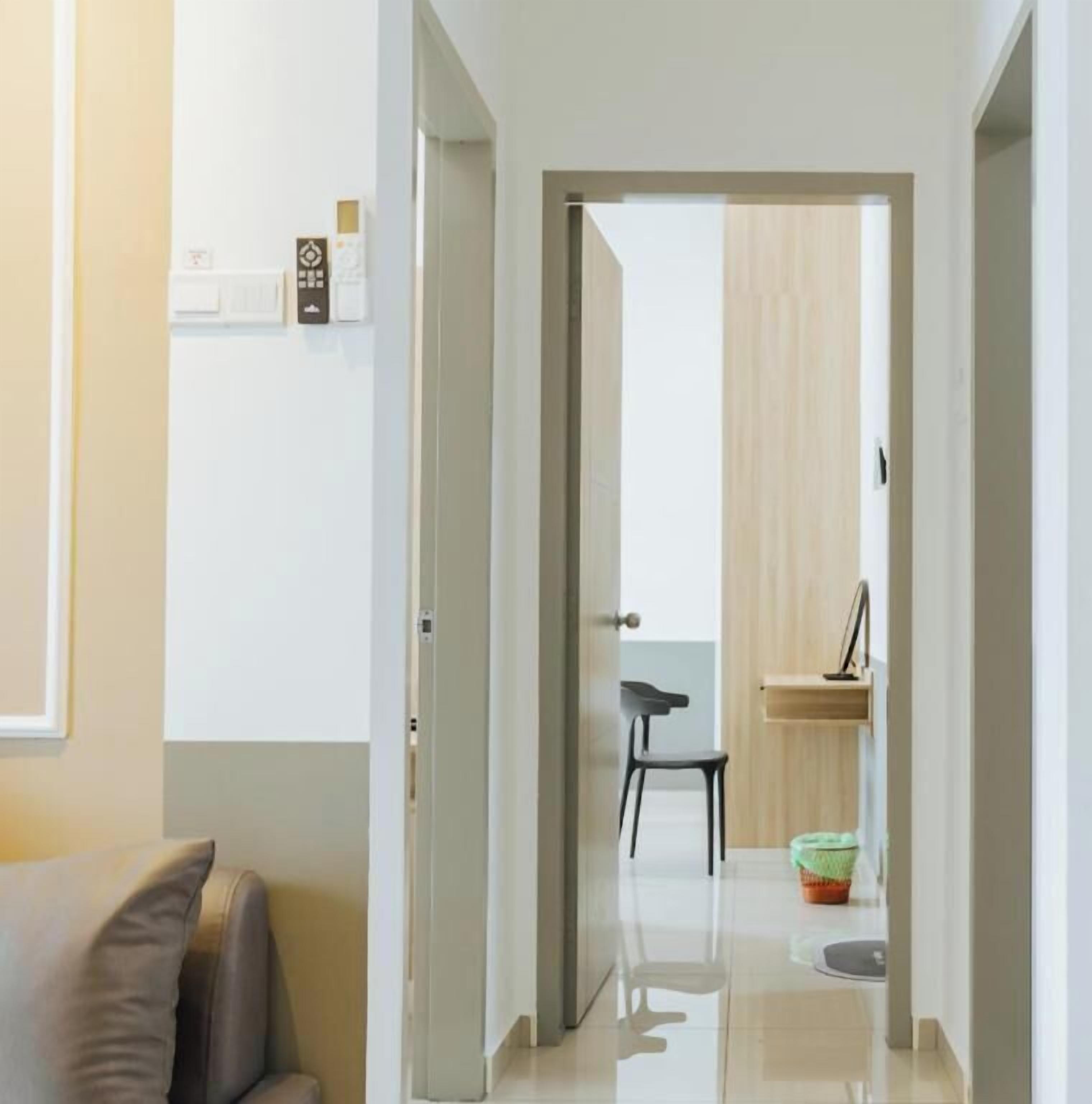 A hallway with a door leading to a room, a chair, a small table, and a trash bin.