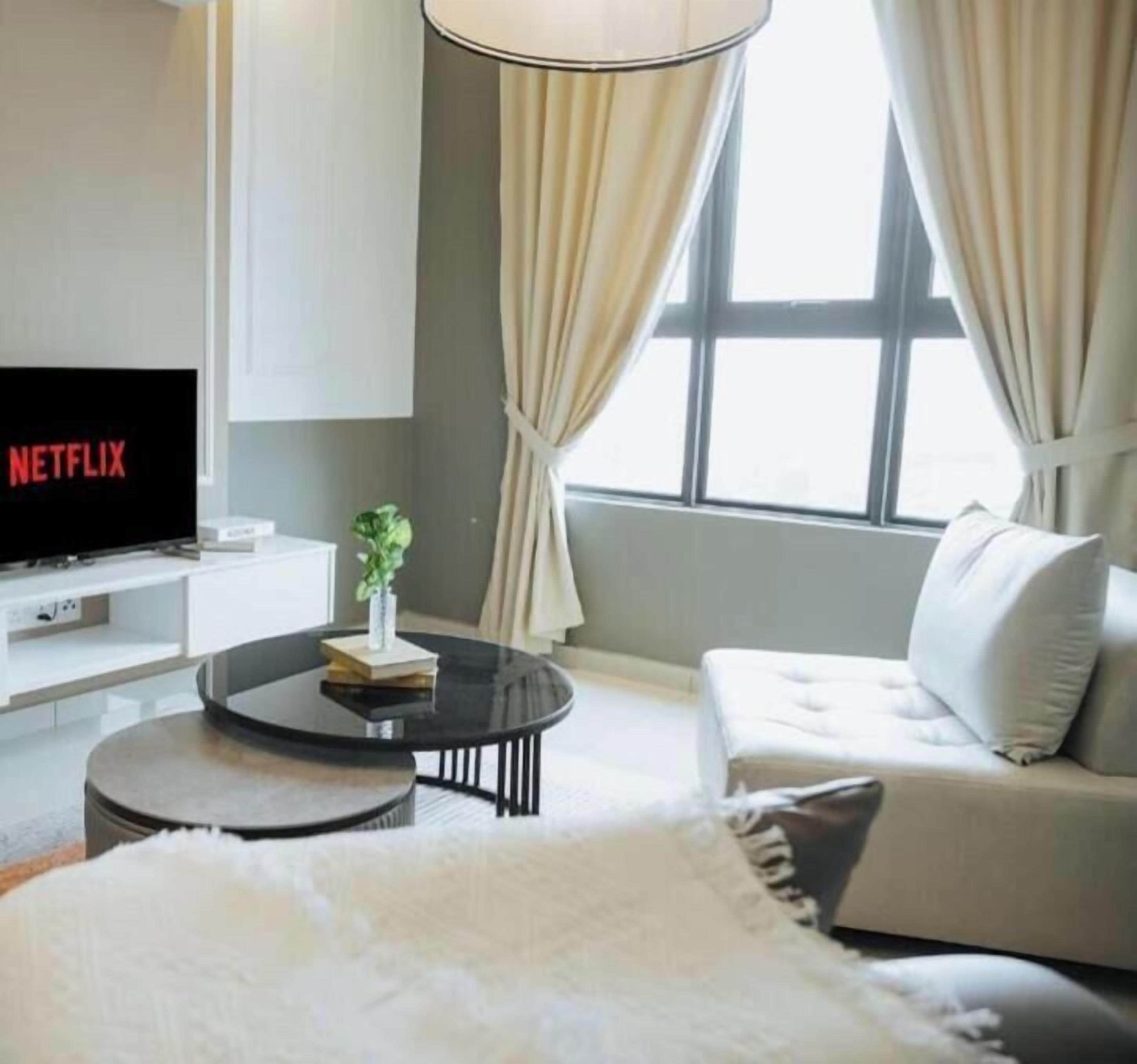 Una sala de estar moderna con un televisor de pantalla plana, una mesa redonda de centro, un sofá y un ventanal con cortinas.
