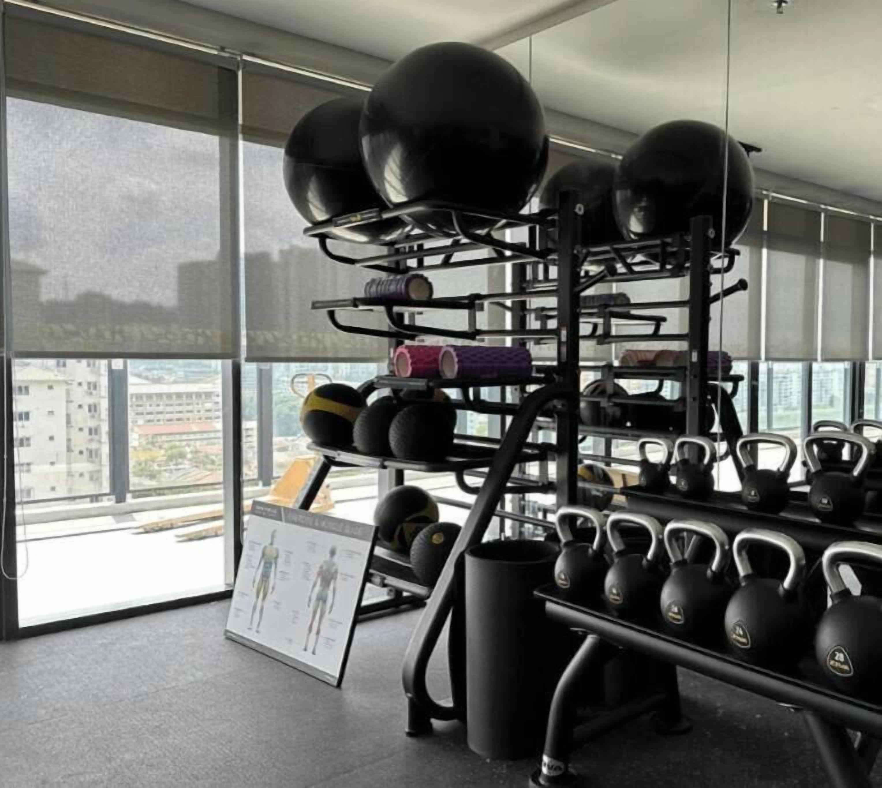 Une salle de sport équipée de kettlebells et de balles lestées rangées sur des étagères, ainsi qu’un présentoir à kettlebells et une affiche accrochée au mur.