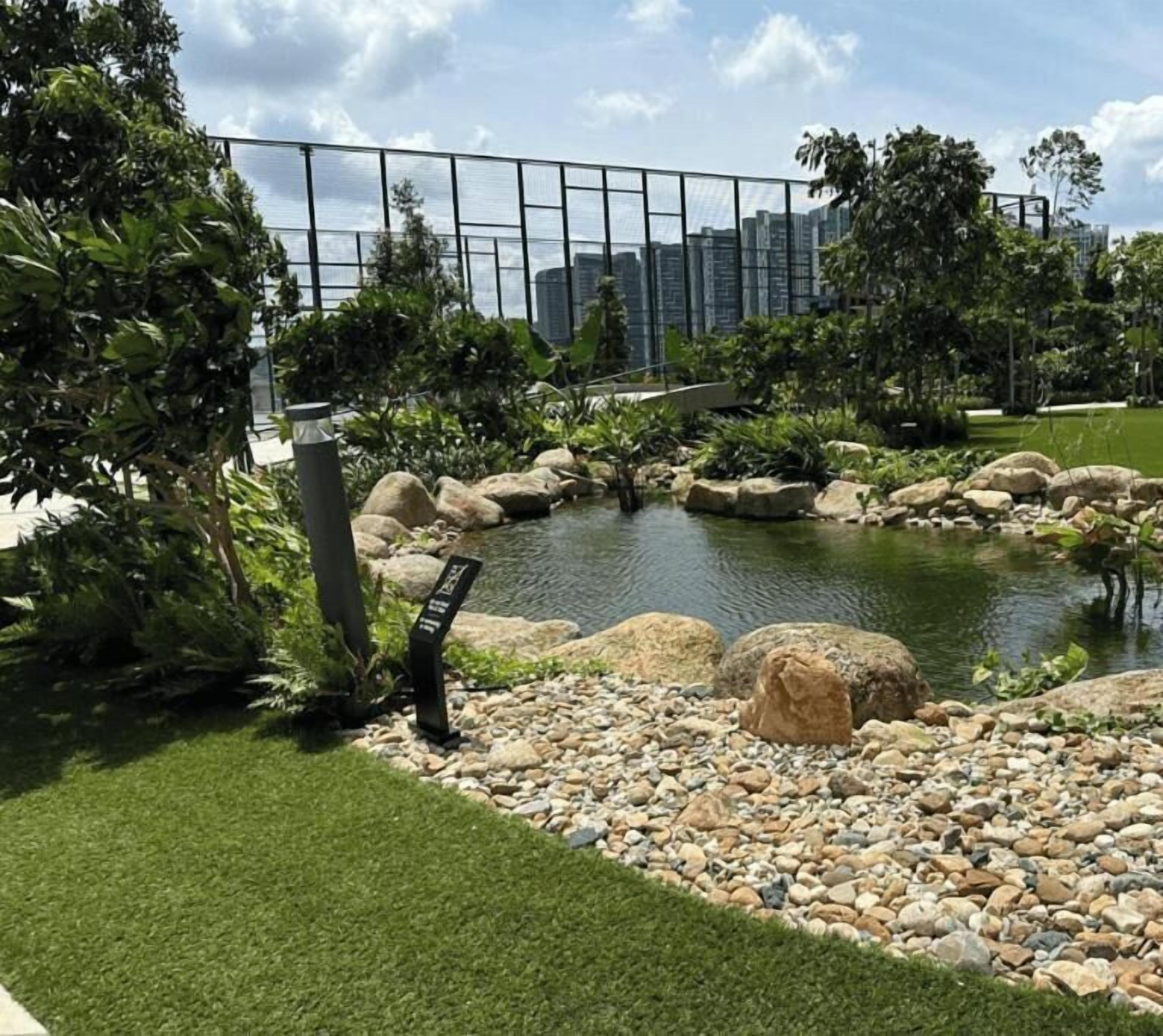 Un jardín ajardinado con un estanque, rocas y una valla.