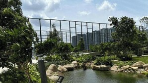 Uma área ajardinada com lago, pedras e vegetação, ao lado de um edifício moderno com janelas de vidro.