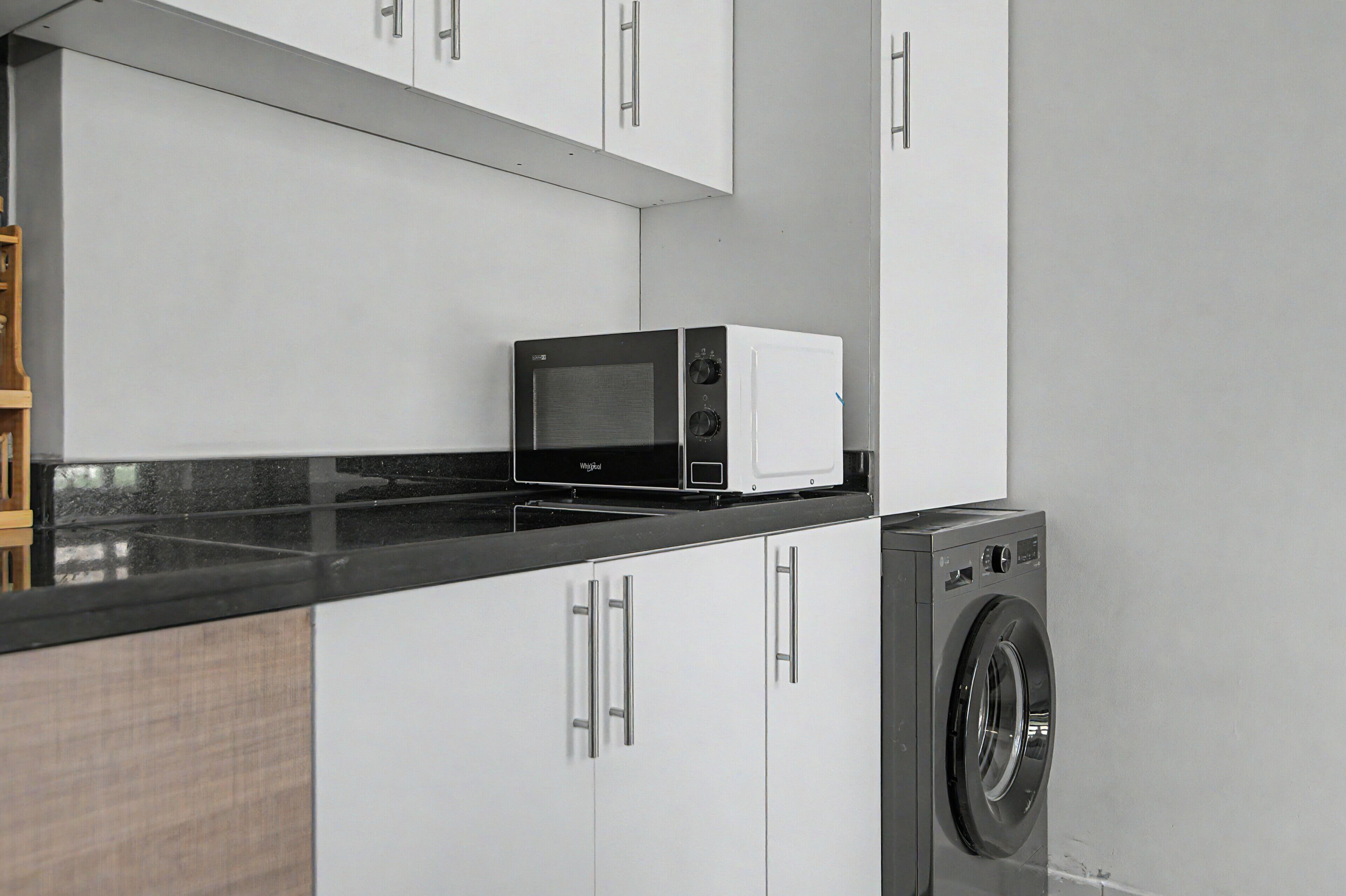 A kitchen with a microwave, a washing machine, and white cabinets.