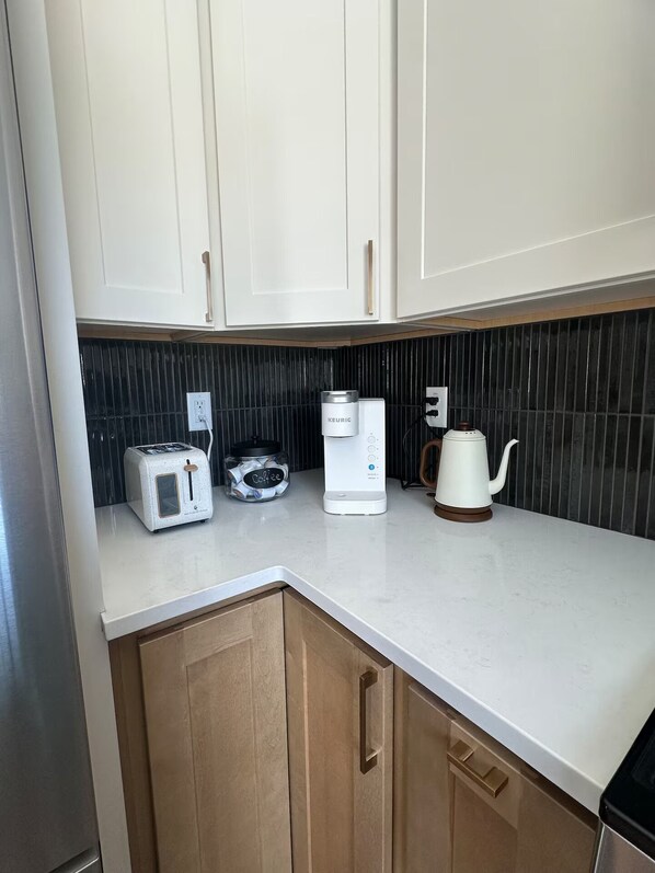 A kitchen with white cabinets, a coffee maker, a kettle, and a toaster.