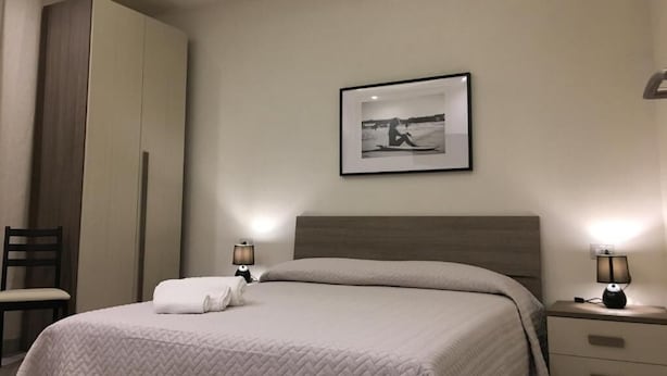 A hotel room with a bed, bedside lamps, a framed picture on the wall, and a chair.