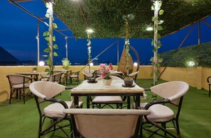 An outdoor dining area with a table set for two, surrounded by chairs, under a covered structure with hanging plants. - pyramids crest hotel (Giza)