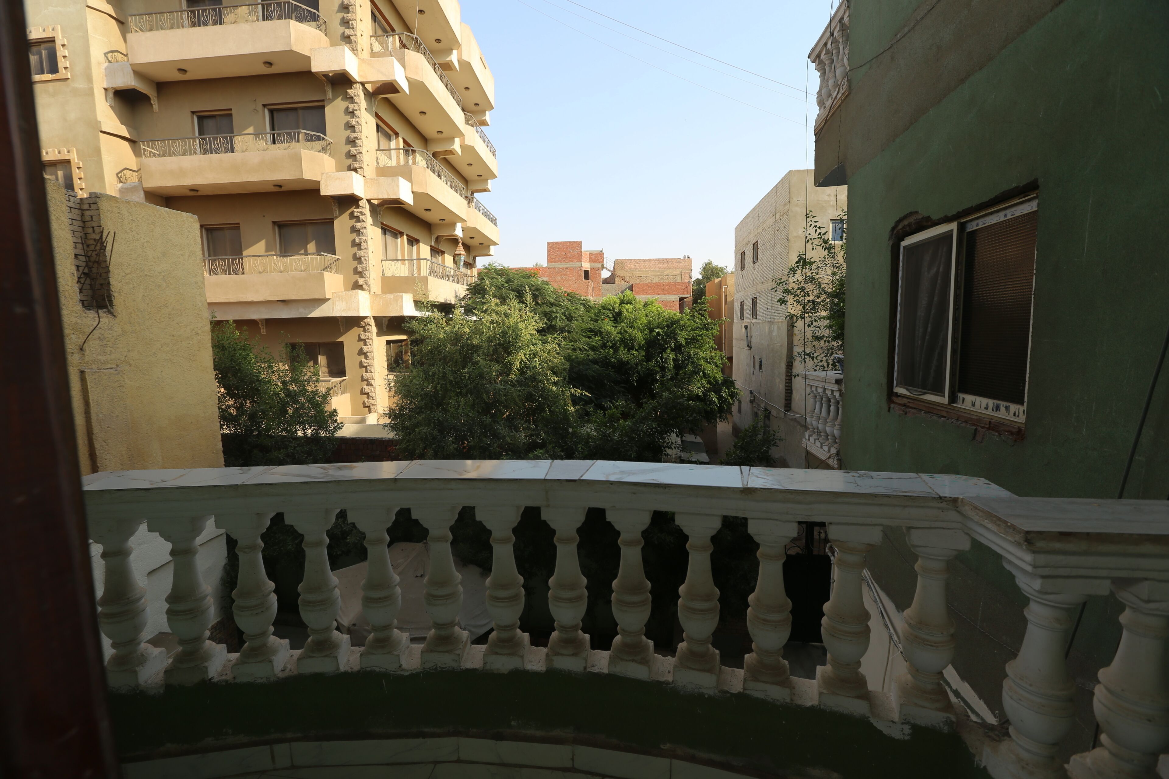 A balcony with a balustrade overlooking a residential area with multi-story buildings and greenery.