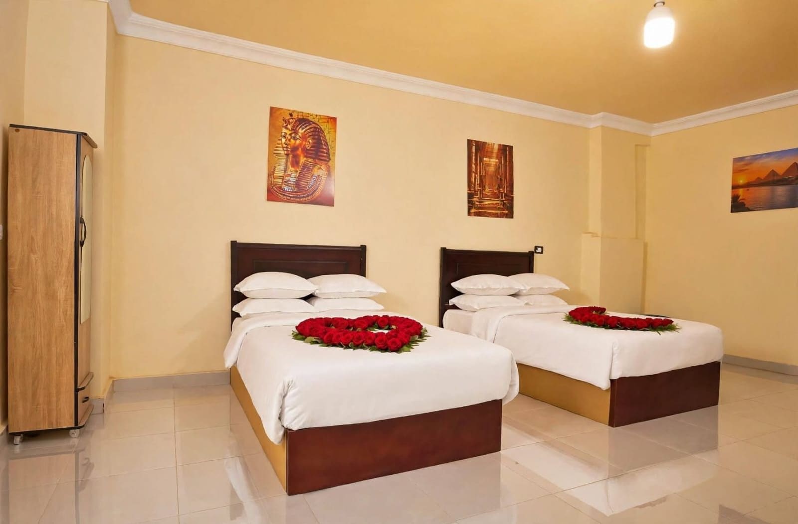 A hotel room with two beds, white linens, and red flower arrangements.