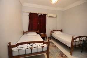 A room with two wooden beds, a small table, a red curtain, and an air conditioning unit on the wall. - pyramids crest hotel (Giza)