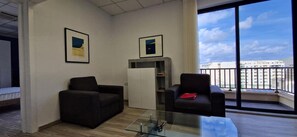 A modern hotel room with a balcony, two armchairs, a glass coffee table, and two framed pictures on the wall. - Enjoy Sliema from this spacious 2-bedroom, 2-bathroom apartment with a private balcony and sea glimpse. With a comfortable living area, equipped kitchen and washing machine, it is ideal for families, couples and longer Malta stays. (Tas-Sliema)
