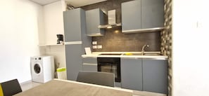 A compact kitchen with grey cabinets, a built-in oven, and a washing machine.