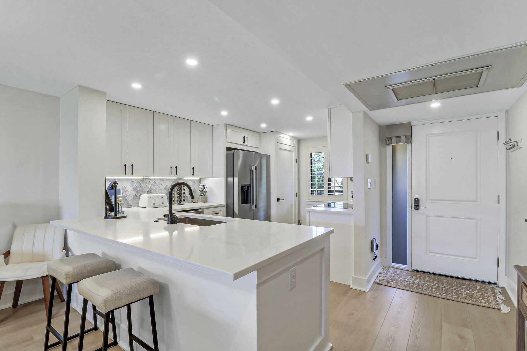 Une cuisine moderne avec des meubles blancs, un îlot central, des appareils en acier inoxydable et un coin bar avec des tabourets.