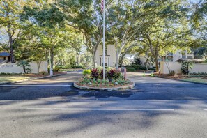 A residential street with a central roundabout, surrounded by trees and a small garden with various plants. - Sunset Rentals | Island Club 3302 (Hilton Head Island)