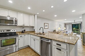 A modern kitchen with stainless steel appliances, a granite countertop, and a view to a balcony. - Sunset Rentals | Colonnade Club 153 (Hilton Head Island)
