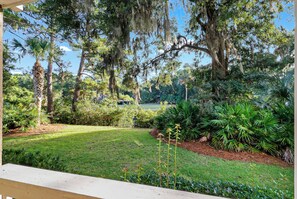 A well-maintained garden with various plants and trees, a clear sky, and a pathway leading to a building. - Sunset Rentals | Colonnade Club 153 (Hilton Head Island)