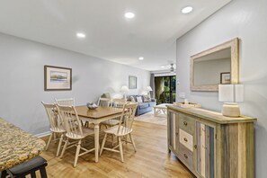 A dining area with a wooden table and chairs, a sofa, and a cabinet with a mirror. - Sunset Rentals | Colonnade Club 153 (Hilton Head Island)
